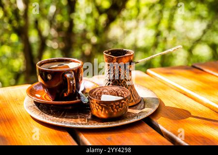 Schwarzer Kaffee in brauner Keramikschale, Vintage-Kupferkaffeekanne und ein Glas mit Zuckerwürfeln auf einem rustikalen Holztisch Stockfoto