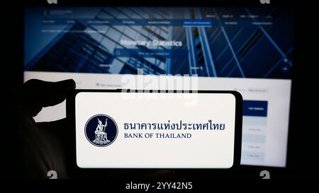 In dieser Abbildung hält eine Person ein Handy mit dem Logo der thailändischen Finanzinstitution Bank of Thailand (BOT) vor der Webseite. Stockfoto