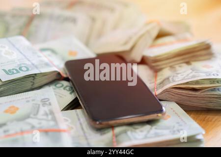 Zugeschnittenes Bild von thailändischen Banknoten und Mobiltelefonen auf einem braunen Holztisch. Selektiver Fokus. Stockfoto