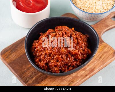 Veganes Tomatenbolognese Ragu mit Sojaproteingranulat in der Schüssel auf Holzbrett auf türkisfarbenem Hintergrund. Einfacher Fleischersatz Sojasauce für Nudeln Stockfoto