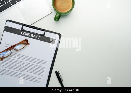 Nahaufnahme des Vertrags auf dem Clipboard, einer Brille, einer Tasse Kaffee und einem Laptop am organisierten Arbeitsplatz Stockfoto