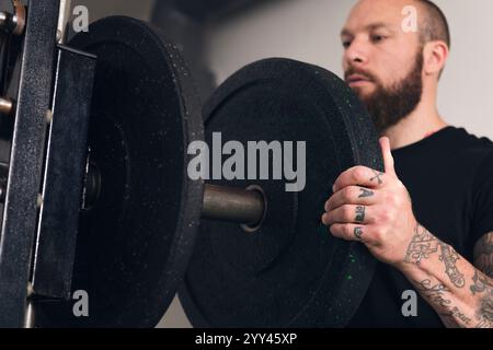 Sportler, der eine Gewichtsplatte auf das Fitnessgerät legt Stockfoto