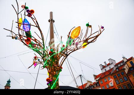 Dekorative Installation, die einem Baum ähnelt, mit Ästen, die mit großen, bunten Glühbirnen und Ornamenten verziert sind. Die Installation ist Teil eines Festes oder h Stockfoto