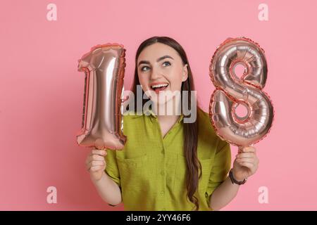 Coming of Age Party - 18. Geburtstag. Glückliche junge Frau mit zahlenförmigen Ballons auf rosa Hintergrund Stockfoto