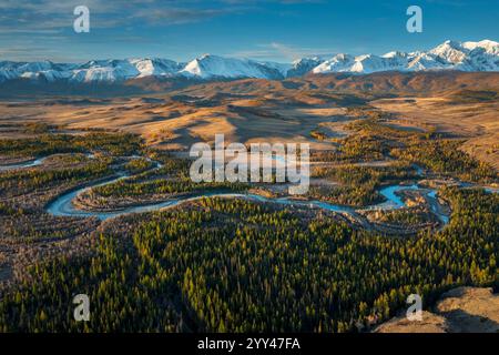 Eine malerische Aussicht auf einen sich windenden Fluss, der durch ein bewaldetes Tal mit schneebedeckten Bergen im Hintergrund fließt, beleuchtet von der warmen Herbstsonne, die ein Gefühl von Ruhe und natürlicher Schönheit weckt Stockfoto