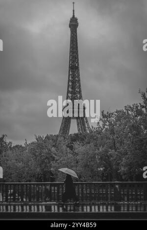 Paris im Regen: Ein monochromer Moment, der die Eleganz des Eiffelturms und eine einsame Figur mit einem Regenschirm einfängt. Stockfoto