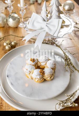 Cremepuffs mit Pralinesahne und Puderzucker auf Weihnachtstisch mit weißer dekorativer Schleife Stockfoto