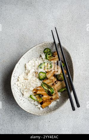 Blick von oben auf ein Gericht mit gegrillten Tofu-Scheiben, die auf einem Bett aus weißem Reis zubereitet und mit scharfen grünen Pfefferscheiben garniert werden. Ein Paar Schwarz Stockfoto