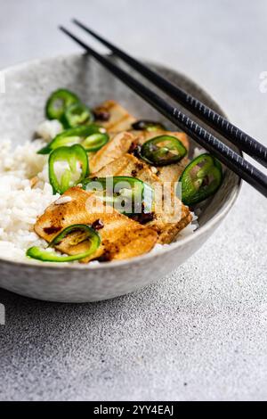 Aus einem Winkel zeigt dieses Bild eine Schüssel mit BBQ-Tofu-Scheiben auf weißem Reis, garniert mit frischen grünen Jalapeno-Scheiben und begleitet von B Stockfoto