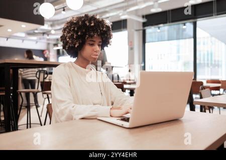 Eine junge Frau mit Vitiligo arbeitet intensiv an einem Laptop in einem trendigen Café. Die Umgebung ist modern und stilvoll, mit natürlichem Licht, das durch l Stockfoto