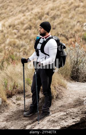 Der schwarze Mann trägt Bergsteiger-Ausrüstung auf einem Wanderweg in Wanderkleidung und steht mit Trekkingstöcken und fängt den Geist des Abenteuers in einer Natur ein Stockfoto