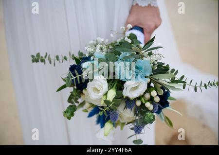 Eine Nahaufnahme eines Brautstraußes mit weißen Rosen, blauen Blumen und üppigem Grün, zart und frisch, perfekt für Eleganz an einem Hochzeitstag Stockfoto