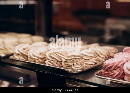 Eine köstliche Auswahl an Gebäck, das elegant in einem Schaufenster präsentiert wird, mit flauschigen Baisons in verschiedenen Farben, perfekt für eine Bäckerei oder ein Konfekt Stockfoto