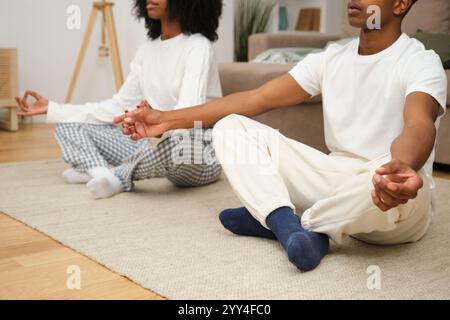 Ein junges Schwarzes Paar meditiert gemeinsam in einer ruhigen häuslichen Umgebung und betont Wellness und Entspannung. Sie sitzen im Kreuz auf einem Teppich und fördern min Stockfoto