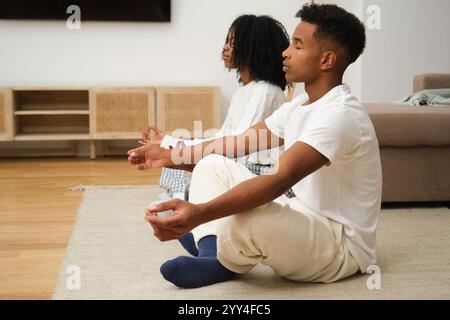 Ein junges schwarzes Paar genießt eine friedliche Meditationssitzung zu Hause, sitzt im Kreuz auf dem Boden in ruhiger Konzentration und schafft ein beruhigendes atmos Stockfoto
