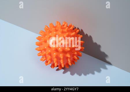 Ein orangefarbener, stacheliger Massageball sitzt auf einem zweifarbigen Hintergrund. Ideal für Muskelentspannung und Fitness als Teil eines therapeutischen Ansatzes. Stockfoto