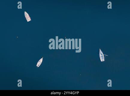 Die Luftperspektive fängt drei weiße Boote ein, die friedlich in ruhigem, tiefblauem Wasser ankern. Eine ruhige Szene, die Ruhe und Freiheit darstellt, perfekt Stockfoto
