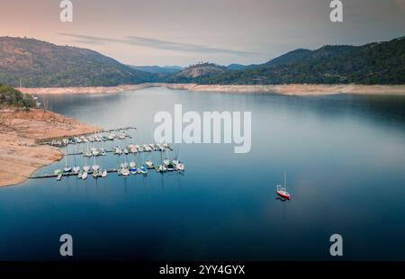 Eine friedliche Seeszene mit Segelbooten entlang der Küste, umgeben von sanften Hügeln und ruhigen Gewässern unter weichem Himmel. Ideal für Natur und Reisen Stockfoto