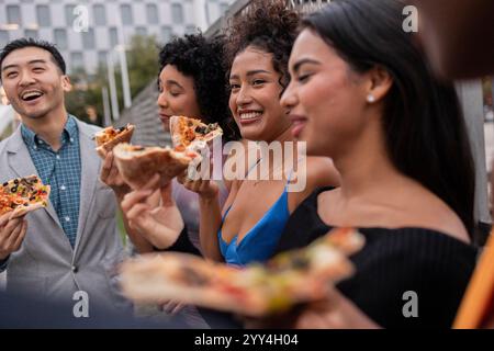 Eine lebhafte Gruppe von Freunden versammelt sich in einer urbanen Umgebung, genießen Pizza und die Gesellschaft des anderen. Die lebhafte Atmosphäre spiegelt Freude und Freundschaft in t wider Stockfoto