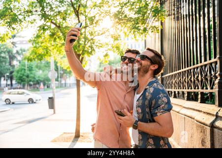 Ein schwules Paar, das einen sonnigen Tag genießt und zusammen mit einem Selfie in einer urbanen Umgebung einen fröhlichen Moment festnimmt Stockfoto