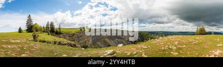 Eine fesselnde Panoramaaufnahme der Creux du Van in Neuchatel, Schweiz, diese atemberaubende Naturfelsenarena ist umgeben von üppigem Grün und dramatischem cl Stockfoto