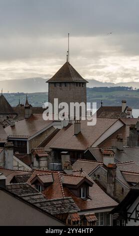 Bezaubernde Aussicht auf alte Terrakottadächer in Murten, Schweiz, mit einem mittelalterlichen Turm unter bewölktem Himmel. Stockfoto