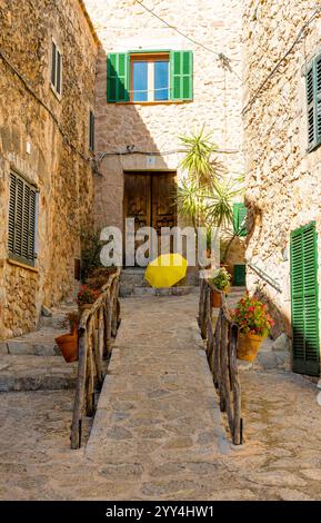 Malerischer Steinweg, flankiert von rustikalen Geländern und lebendigen Blumentöpfen unter der mediterranen Sonne, mit einem hellgelben Regenschirm, in Valldemosa Stockfoto