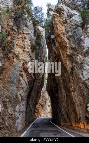 Eine schmale Straße schlängelt sich durch hoch aufragende Felsformationen in Mallorca, Spanien. Die ruhige Szene fängt die natürliche Schönheit und dramatische Landschaft dieser Region ein Stockfoto
