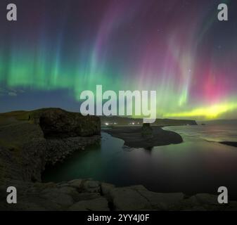 Ein atemberaubender Blick auf die aurora Borealis, die den Nachthimmel über Dyrholaey, Island, erleuchtet. Die lebendigen Farben spiegeln sich auf dem Wasser unter sich und schaffen so Stockfoto