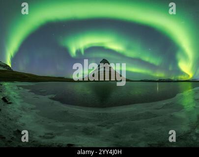 Die atemberaubende Aurora Borealis beleuchtet den Nachthimmel über dem berühmten Kirkjufell Mountain und reflektiert auf dem eisigen Wasser unter Einem atemberaubenden Blick auf Stockfoto