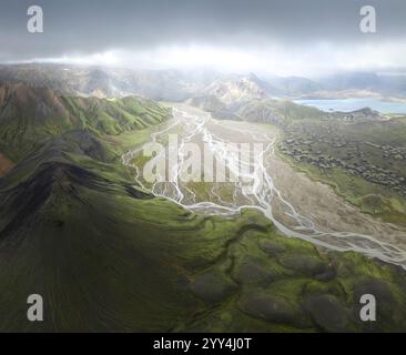 Eine atemberaubende Luftaufnahme von Islands riesigem Flusstal umgeben von üppigen grünen Bergen unter einem dramatischen Himmel. Die lebendige Landschaft zeigt die Natur. Stockfoto