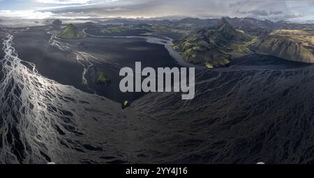 Ein atemberaubender Blick aus der Luft auf Islands dramatische Landschaft mit gewundenen Flüssen, üppigen grünen Bergen und vulkanischem Gelände unter einem dynamischen, bewölkten s Stockfoto