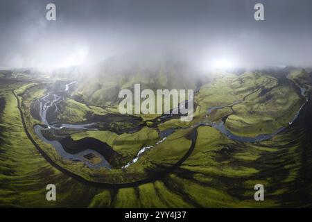 Ein atemberaubender Blick aus der Vogelperspektive auf Islands üppiges grünes Hochland mit gewundenen Flüssen und umhüllendem Nebel verströmt die dramatische Landschaft ein mystisches an Stockfoto