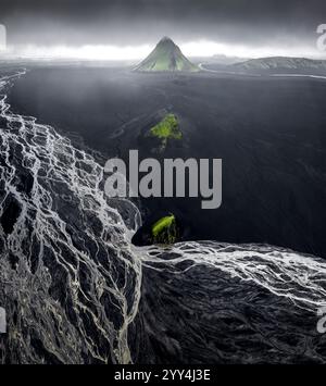 Atemberaubende Aussicht auf Islands dramatische Landschaft mit einem konischen vulkanischen Berg, umgeben von dunklen Ebenen und einem komplizierten, netzartigen Fluss Stockfoto