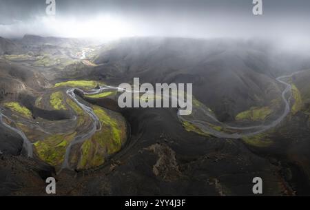 Ein atemberaubender Blick aus der Vogelperspektive fängt Islands raues Gelände ein, mit gewundenen Flüssen und lebendigem grünem Moos vor dunklem vulkanischem Boden unter einem Dramat Stockfoto