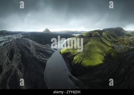 Atemberaubende Aussicht aus der Vogelperspektive auf Islands zerklüftete Landschaft mit schlängelnden Flüssen, üppigen grünen Hügeln und dramatischen Bergen unter einem stimmungsvollen Himmel, Showcas Stockfoto