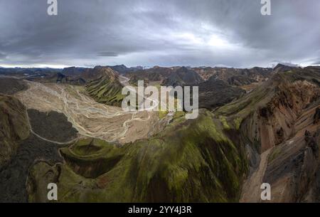 Ein atemberaubender Blick aus der Luft zeigt Islands raues Gelände mit üppigen Tälern, gewundenen Flüssen und vulkanischen Bergen unter einem weitläufigen bewölkten Himmel Stockfoto