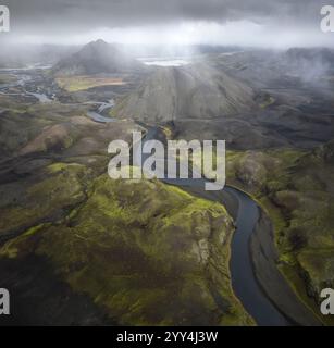 Blick aus der Vogelperspektive auf Islands atemberaubende Landschaft mit gewundenen Flüssen, die durch üppige grüne Täler und majestätische Berge unter einem dramatischen, Stockfoto