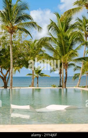 Ruhiges Bild eines klaren, ruhigen Pools mit umliegenden Palmen und atemberaubendem Meerblick im Hintergrund, ideal für Reisen und Entspannung Stockfoto