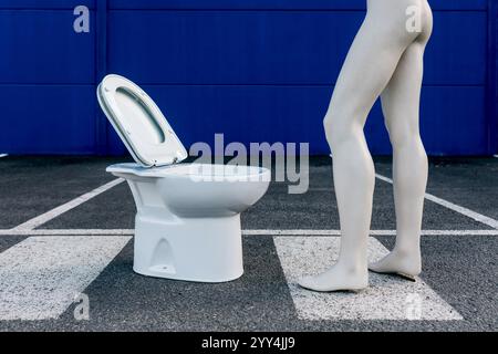 Eine humorvolle Kunstszene zeigt eine männliche Schaufensterpuppe, die vor einer Toilette auf einem Parkplatz steht. Der auffällige blaue Hintergrund steht im Kontrast zum Mann Stockfoto