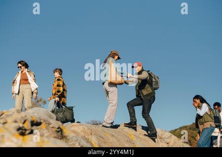 Eine junge Frau hilft einem männlichen Freund, den Berg gegen den blauen Himmel zu klettern Stockfoto