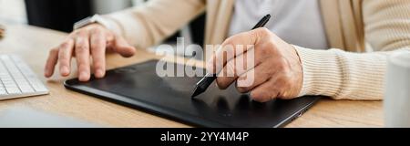Ein gutaussehender älterer Mann zeichnet auf einem Tablet, während er an einem stilvollen Holztisch sitzt. Stockfoto