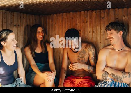 Glückliche multirassische Freunde, die in der Holzsauna sitzen Stockfoto