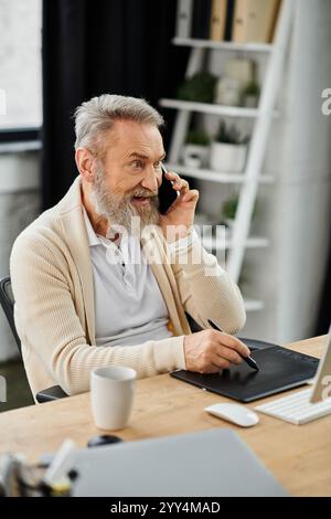Hübscher älterer Mann, der am Telefon mit einem Lächeln spricht, während er an seinem stilvollen Schreibtisch saß Stockfoto