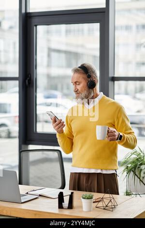 Ein reifer, gutaussehender Mann mit Bart hört Musik über Kopfhörer, während er eine Kaffeetasse hält. Stockfoto