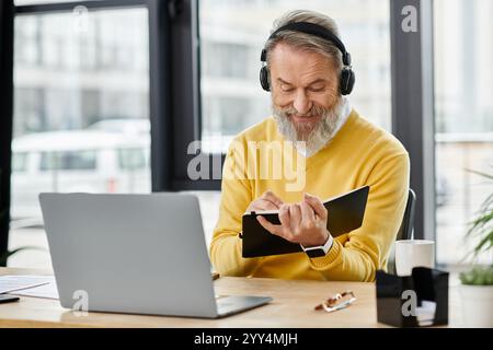 Gutaussehender reifer Mann mit Kopfhörern schreibt Notizen, während er an einem Schreibtisch in einem modernen Café sitzt. Stockfoto