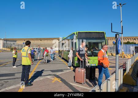 Civitavecchia, Italien - 19. Dezember 2024: Passagiere steigen an einem Terminal aus, wobei das Personal in Warnwesten ihnen beim Gepäckwagen hilft Stockfoto