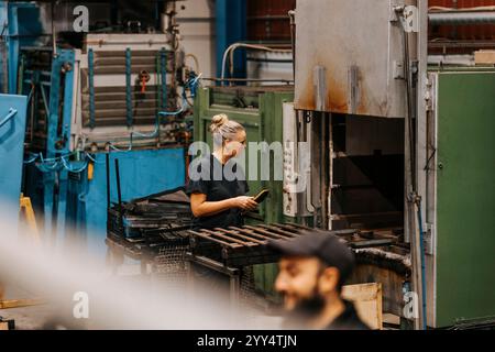 Fokussierte, ausgereifte Fabrikarbeiterin, die die Maschine bedient, während sie die Fernbedienung hält Stockfoto