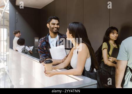 Glücklicher männlicher Student, der mit einer Freundin spricht, während er im Flur des Colleges steht Stockfoto