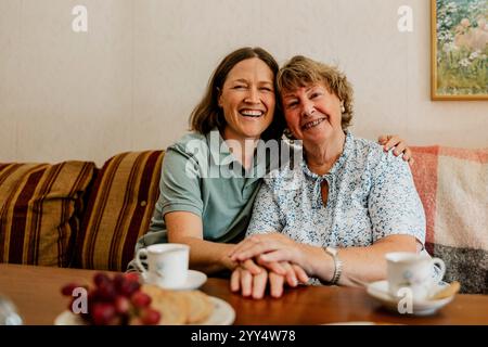 Porträt einer glücklichen Seniorin, die mit einer Krankenschwester im Wohnzimmer zu Hause sitzt Stockfoto